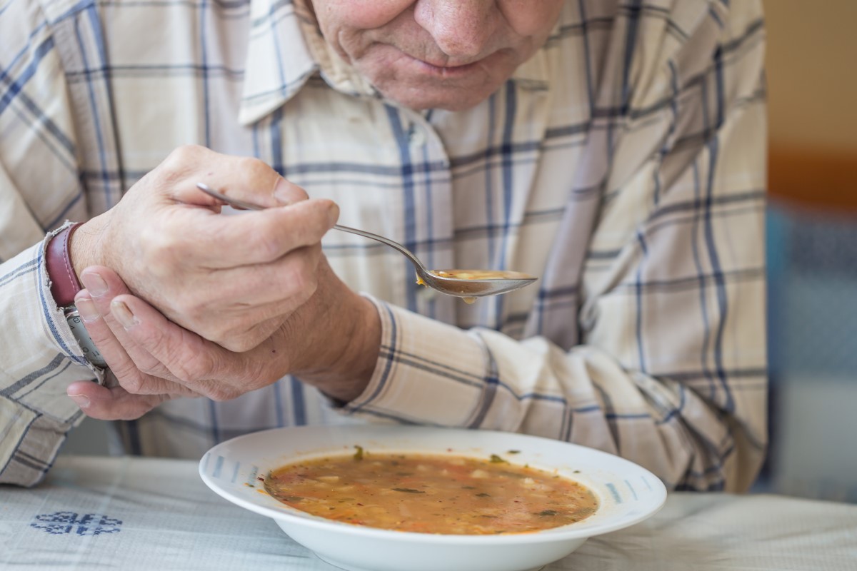 Mies syö keittoa ja pitää kädestä kiinni Parkinsonin taudin vapinaa vastaan