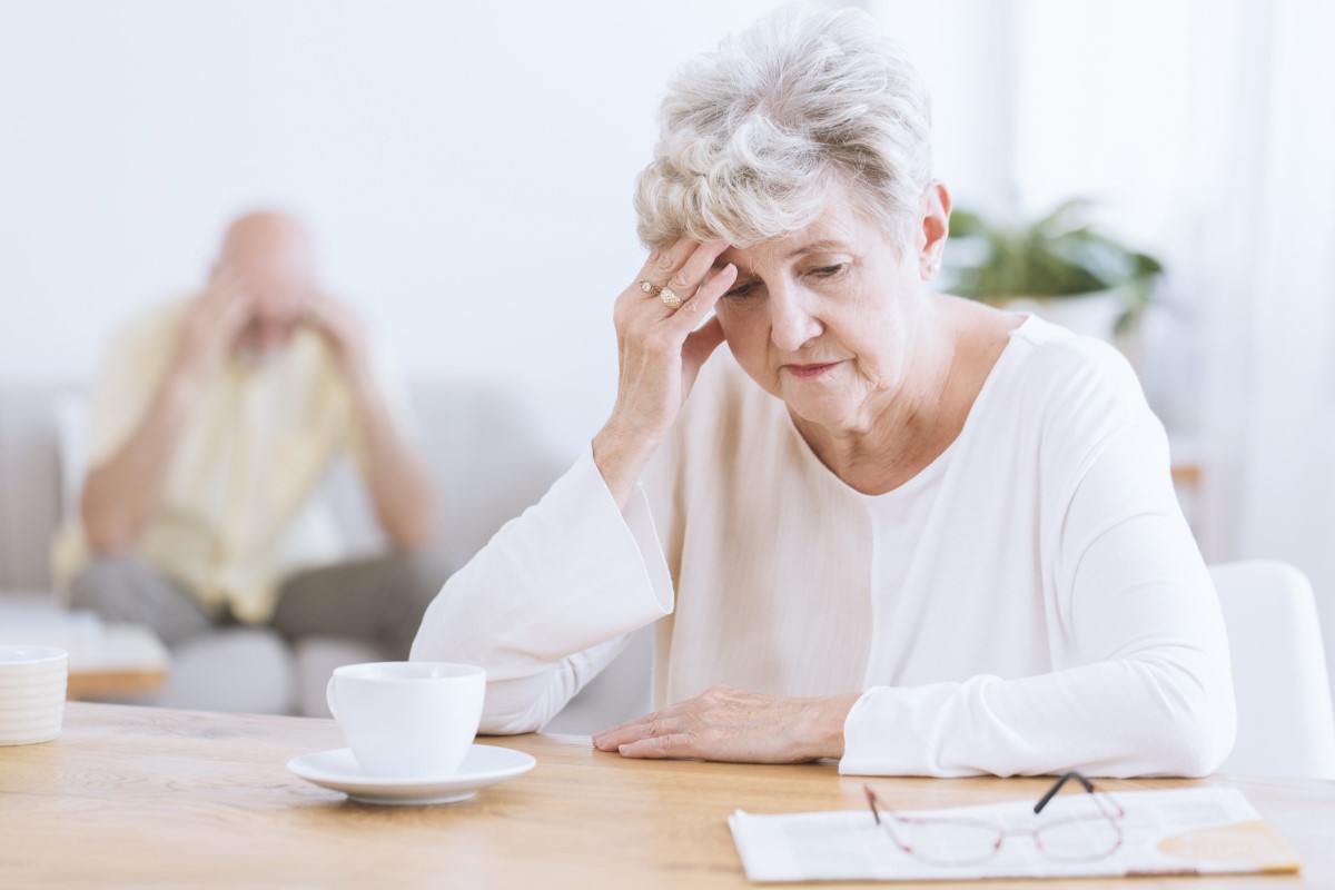 Iäkäs nainen pitelee päätään, koska aivojen neurologiset toiminnot ovat heikentyneet, mahdollisesti Alzheimerin tauti. Iäkäs nainen etualalla, pää kumarassa, nojaa käteensä.