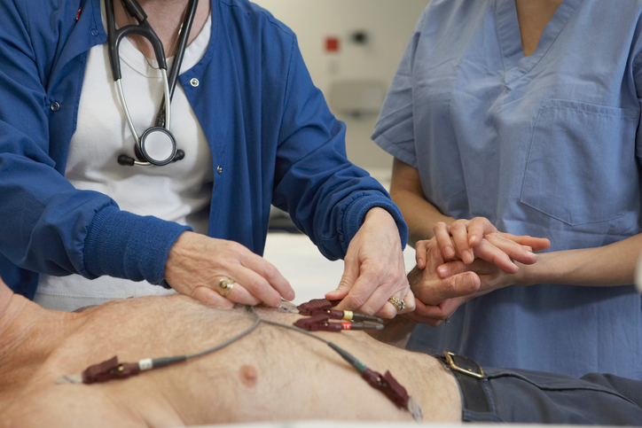 Miehen EKG-tutkimus, elektrodit hänen rinnassaan, kaksi lääkäriä tutkii häntä.